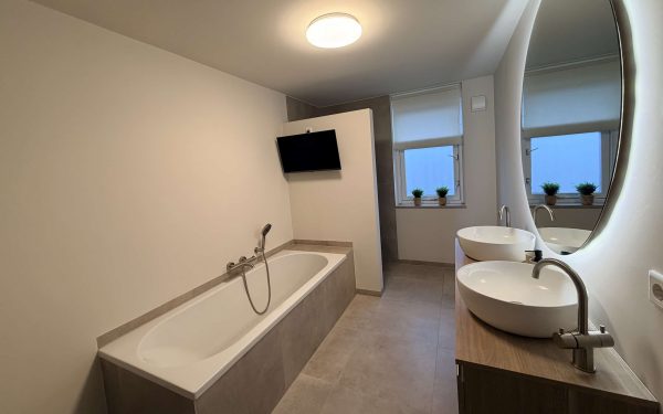 Ruime badkamer in Best met inbouwbad, dubbele waskom op houten meubel en grote ovale ledspiegel