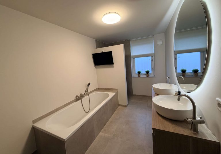Ruime badkamer in Best met inbouwbad, dubbele waskom op houten meubel en grote ovale ledspiegel