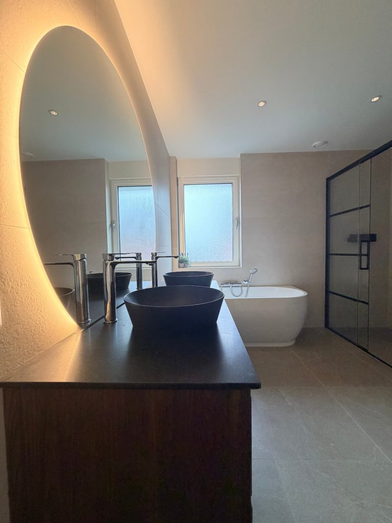 Vrijstaand wit bad bij raam met grootformaat marmerlook tegels en zwart wastafelblad in luxe badkamer Waalre