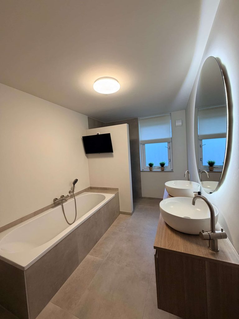 Moderne badkamer in Best met betonlook tegelwerk, ledspiegel en TV aan de wand