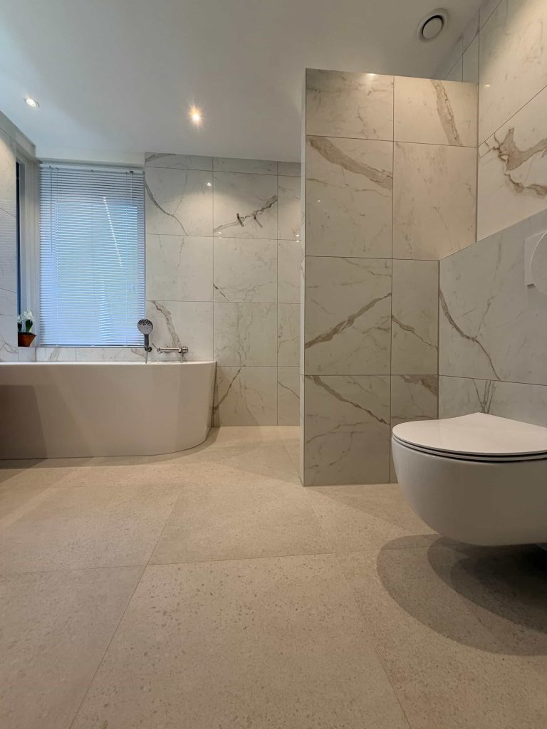 Overzicht van een lichte marmerlook badkamer met halfvrijstaand bad, zwevend houten meubel en hangend toilet