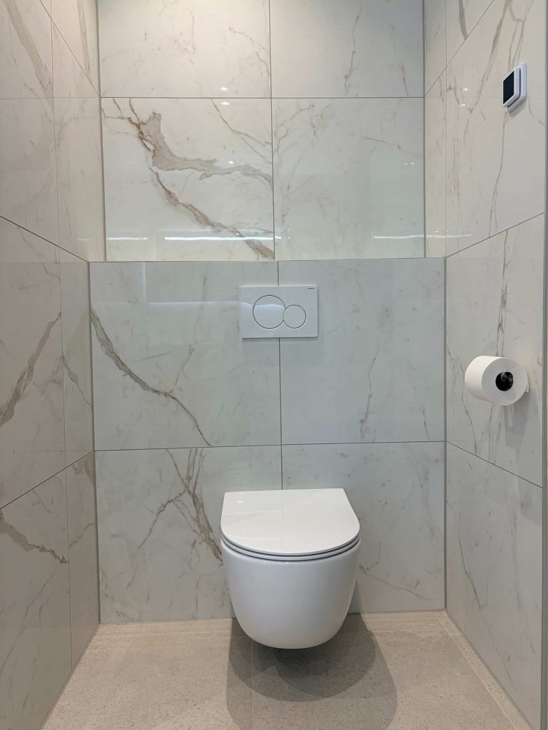 Hangend toilet in een nis van glanzende marmerlook tegels met witte bedieningsplaat