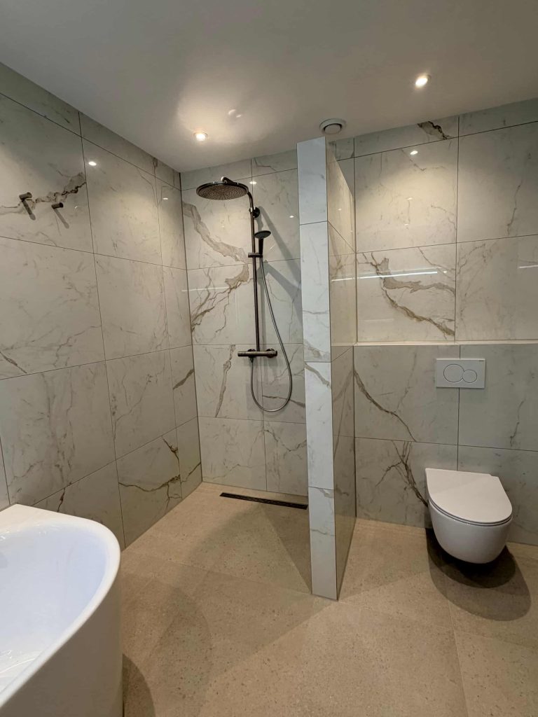 Inloopdouche met regendouche en marmerlook scheidingswand naast een hangend toilet en natuursteenlook vloer
