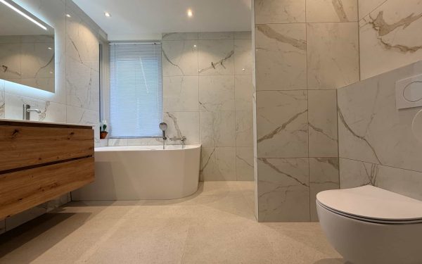 Overzicht van een lichte marmerlook badkamer met halfvrijstaand bad, zwevend houten meubel en hangend toilet