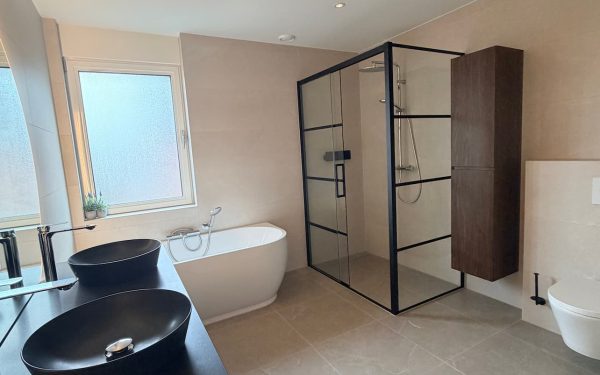 Luxe badkamer in Waalre met halfvrijstaand hoekbad, inloopdouche en dubbele natuurstenen waskom op donker houten meubel