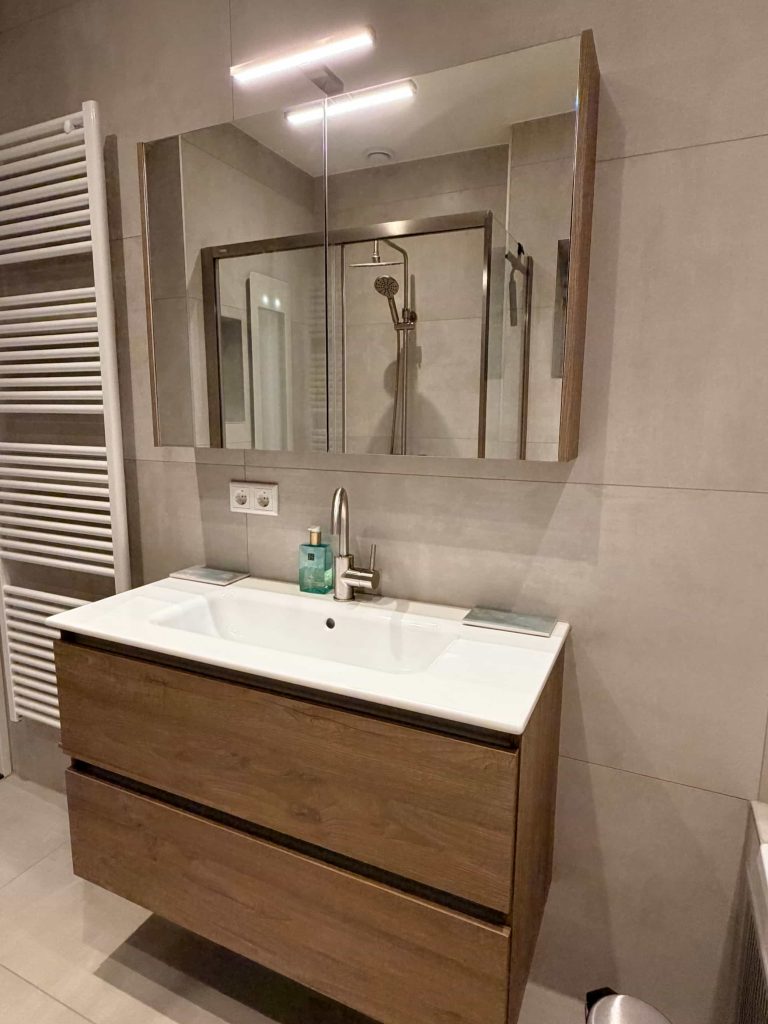 Houtlook badkamermeubel met spiegelkast en RVS-look kraan in compacte badkamer in Eindhoven