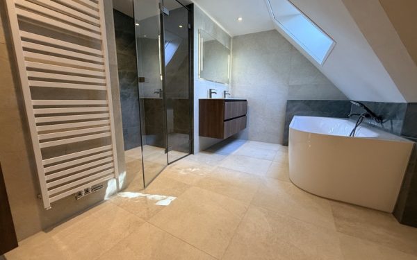 Badkamer met half vrijstaand bad, inloopdouche en dubbele wastafel onder een schuine wand