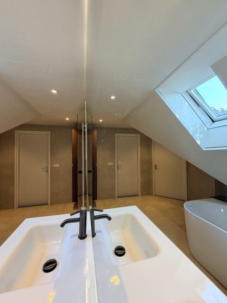 Ruime badkamer met breed wastafelblad, spiegelwand en half vrijstaand bad bij het dakraam