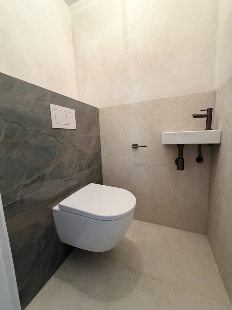 Apart toilet in de badkamer met wandcloset, fonteintje en groene tegelwand