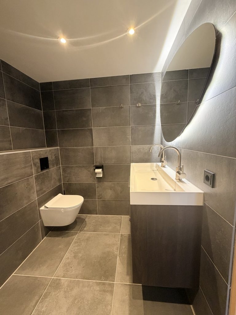 Hangtoilet en brede wastafel met organische spiegel in een betonlook badkamer