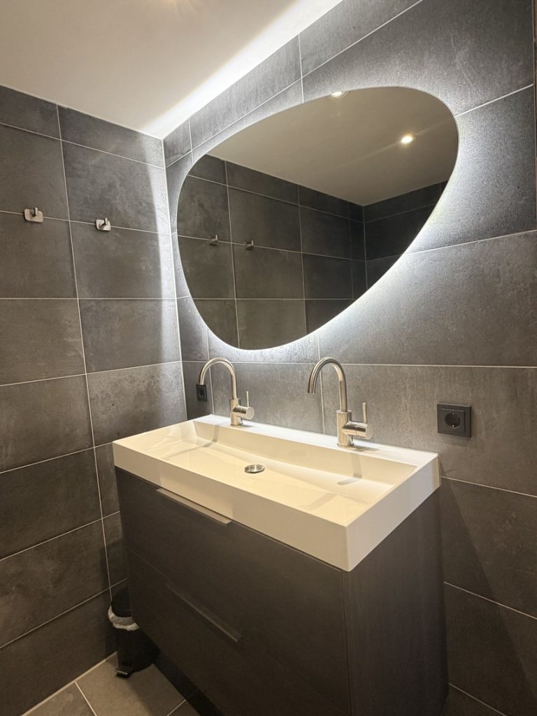 Brede wastafel met twee kranen op een donker houtlook badmeubel