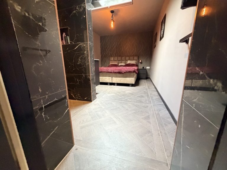 Doorkijk vanuit de inloopdouche naar de slaapkamer met doorlopende houtlook vloertegels